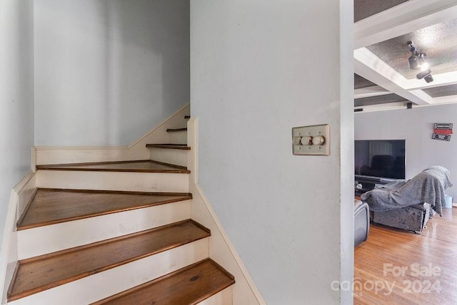 staircase featuring a textured ceiling, beamed ceiling, and hardwood / wood-style flooring