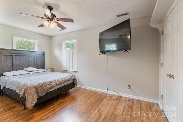 bedroom with light wood-type flooring, a closet, ceiling fan, and a textured ceiling