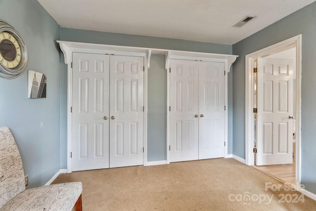 unfurnished bedroom with a textured ceiling, light carpet, and multiple closets