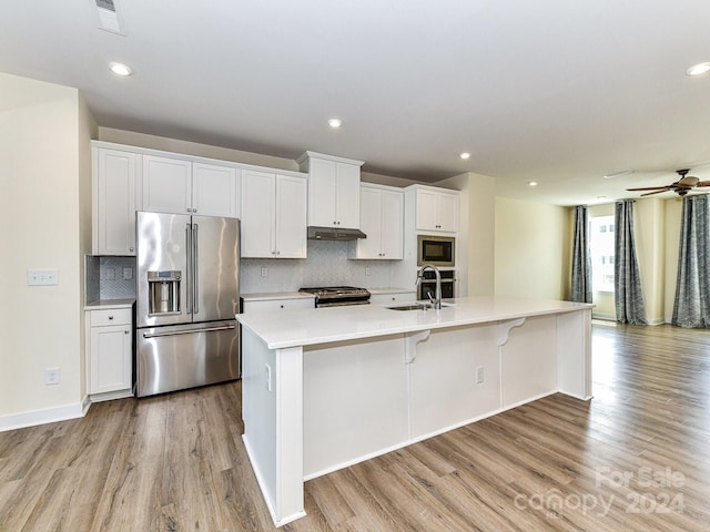 kitchen featuring light hardwood / wood-style flooring, appliances with stainless steel finishes, white cabinetry, ceiling fan, and a center island with sink