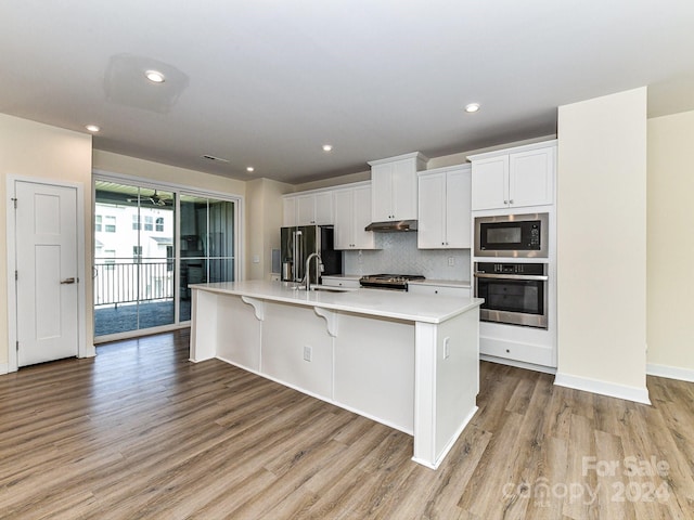 kitchen with light hardwood / wood-style flooring, appliances with stainless steel finishes, white cabinetry, a spacious island, and a breakfast bar area