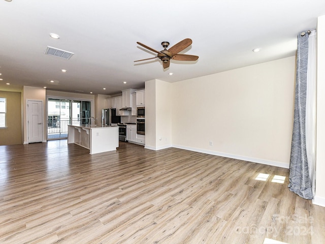 unfurnished living room featuring ceiling fan, light hardwood / wood-style floors, and sink