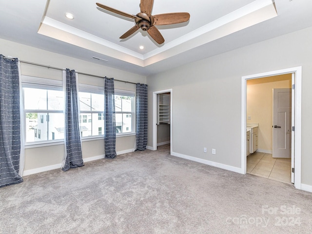 unfurnished bedroom featuring light colored carpet, ceiling fan, ensuite bath, and a tray ceiling