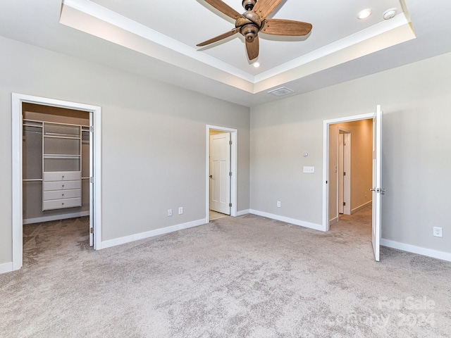 unfurnished bedroom with light colored carpet, a walk in closet, a tray ceiling, a closet, and ceiling fan