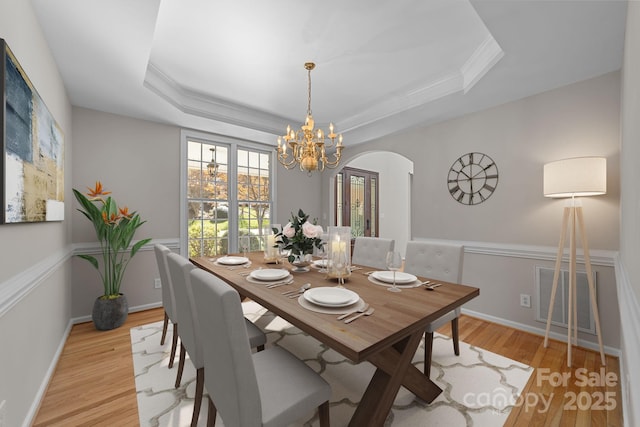 dining room with a raised ceiling, crown molding, light hardwood / wood-style floors, and a notable chandelier