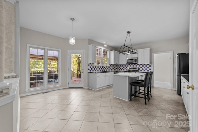 kitchen with stainless steel appliances, light tile patterned floors, a center island, white cabinetry, and hanging light fixtures