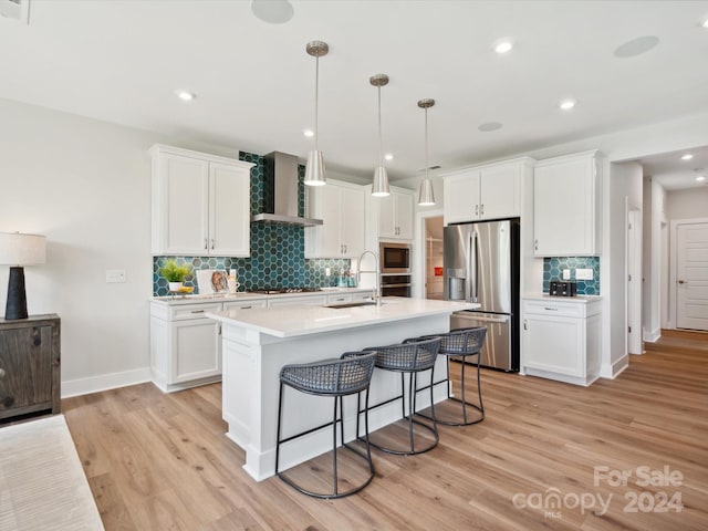 kitchen with a breakfast bar area, a sink, stainless steel appliances, light countertops, and wall chimney range hood