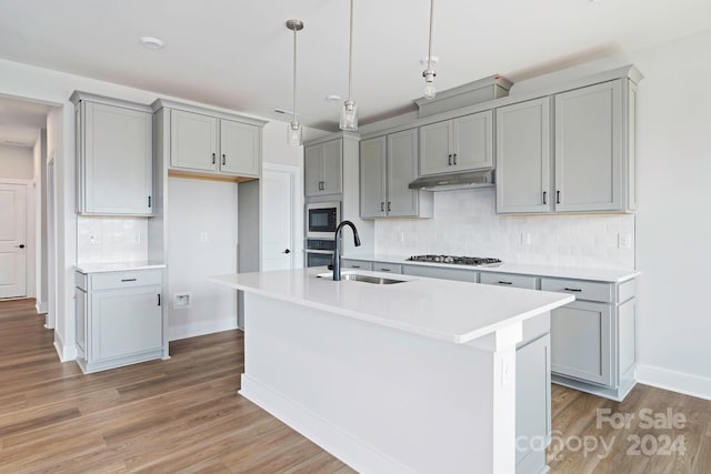 kitchen with gray cabinetry, under cabinet range hood, light wood-type flooring, appliances with stainless steel finishes, and a sink