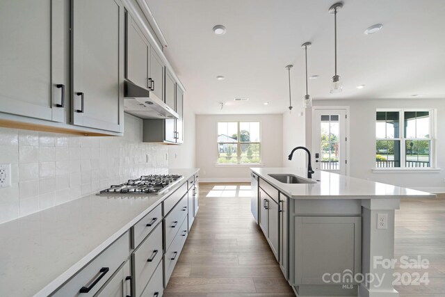 kitchen featuring gray cabinetry, a center island with sink, pendant lighting, sink, and light wood-type flooring