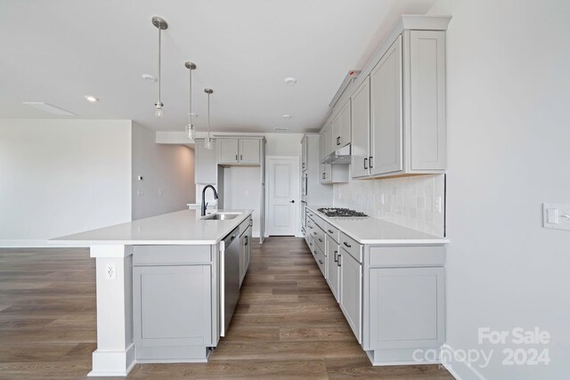 kitchen with decorative light fixtures, hardwood / wood-style floors, stainless steel appliances, sink, and a kitchen island with sink