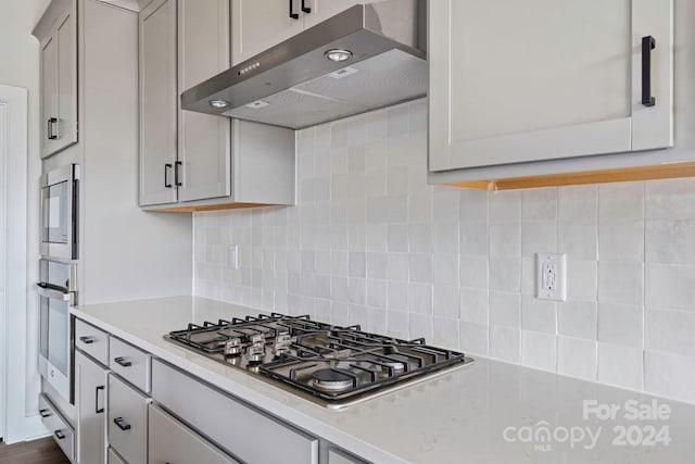 kitchen featuring gray cabinets, appliances with stainless steel finishes, light stone countertops, and tasteful backsplash