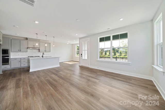 kitchen featuring a kitchen island with sink, hanging light fixtures, gray cabinets, gas cooktop, and hardwood / wood-style flooring