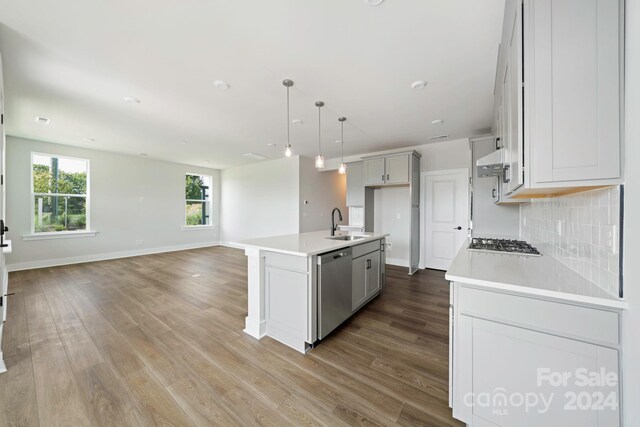 kitchen featuring hanging light fixtures, stainless steel appliances, sink, wood-type flooring, and an island with sink