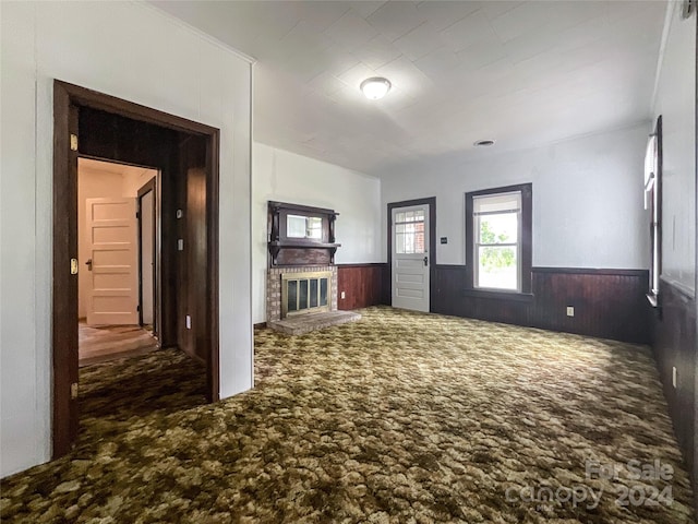 unfurnished living room with a brick fireplace, wooden walls, and dark carpet