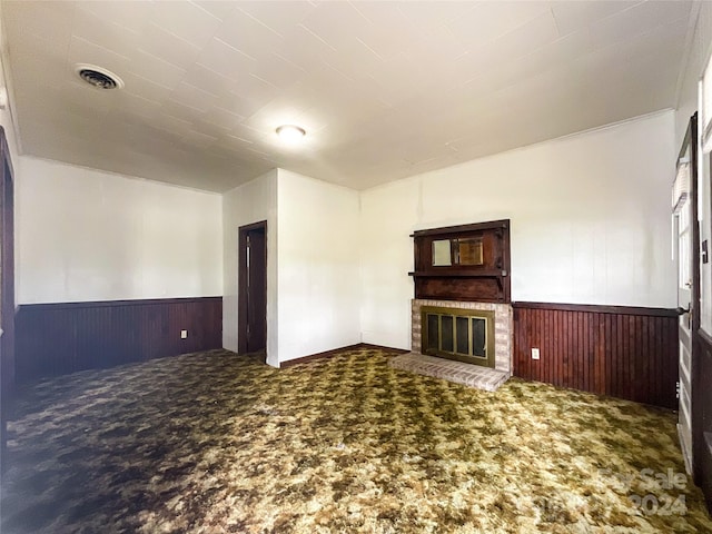 unfurnished living room featuring a brick fireplace, carpet, and wooden walls