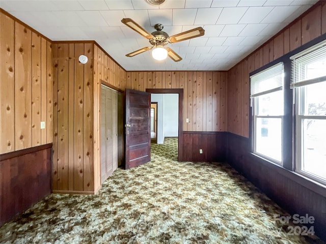 carpeted empty room with wooden walls and ceiling fan