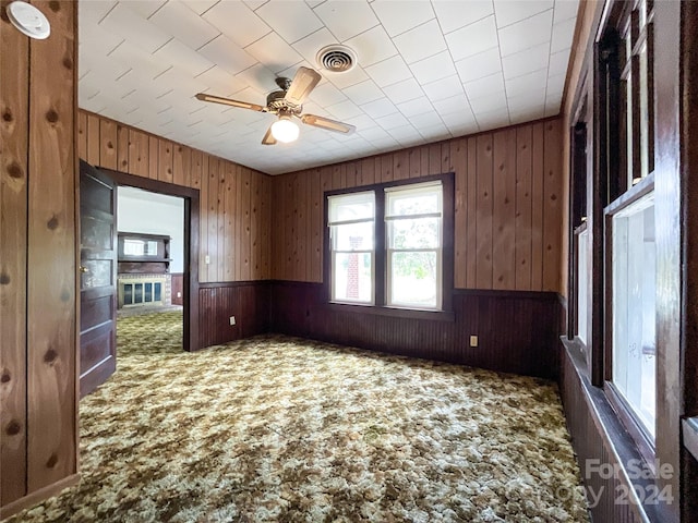 unfurnished room with ceiling fan, wood walls, and dark carpet