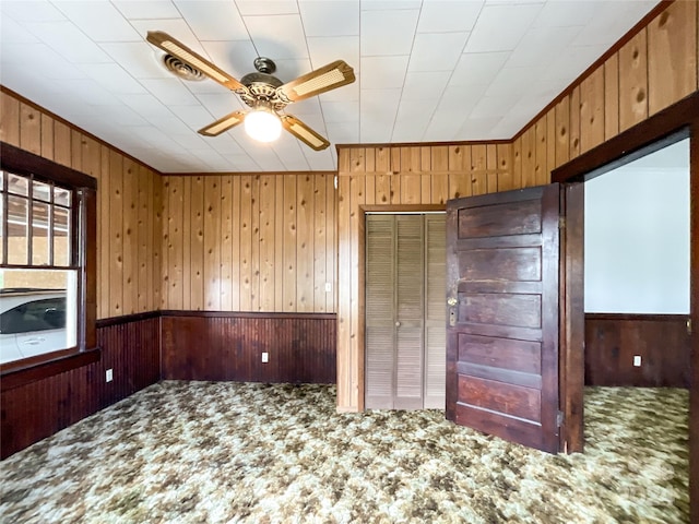 unfurnished bedroom featuring wood walls, a closet, carpet floors, and ceiling fan