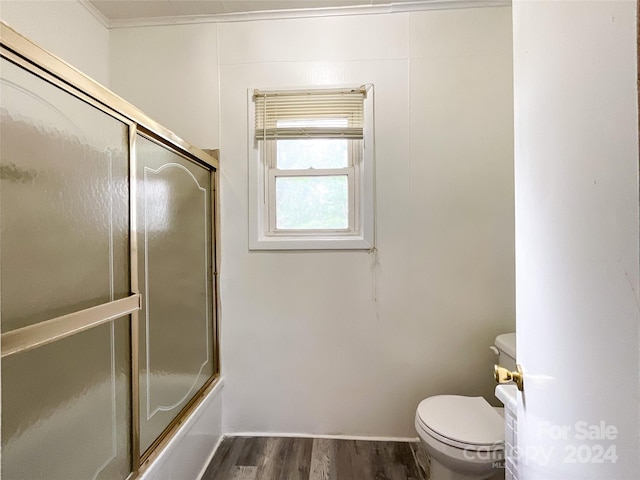 bathroom with wood-type flooring, ornamental molding, combined bath / shower with glass door, and toilet