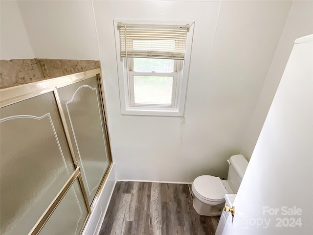 bathroom with hardwood / wood-style flooring, an enclosed shower, and toilet