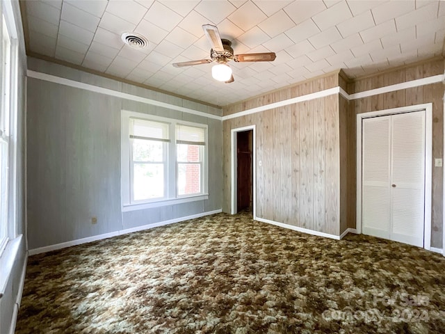 unfurnished bedroom with carpet, wooden walls, and ceiling fan