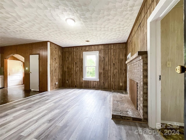 additional living space with a brick fireplace, wood walls, hardwood / wood-style floors, and a textured ceiling