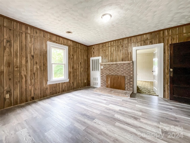 unfurnished living room with wood walls, light wood-type flooring, and a textured ceiling