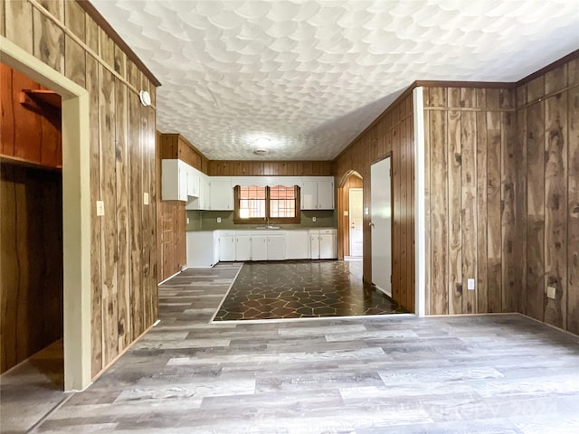 kitchen with wooden walls, sink, wood-type flooring, and white cabinets