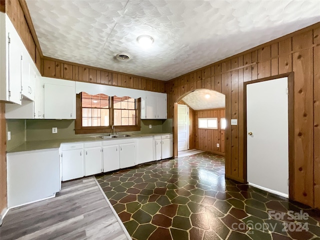 kitchen with wooden walls, dark wood-type flooring, sink, white cabinetry, and a textured ceiling