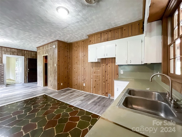 kitchen featuring white cabinets, sink, wood walls, and hardwood / wood-style floors