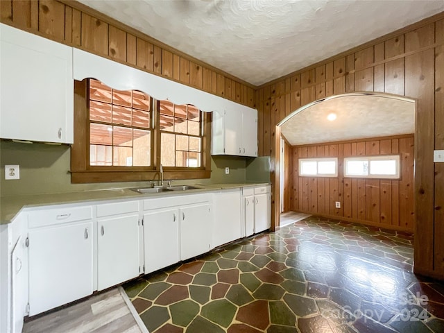 kitchen featuring wooden walls, white cabinetry, sink, and a textured ceiling