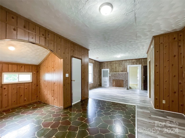 additional living space with wood walls, a fireplace, lofted ceiling, and a textured ceiling