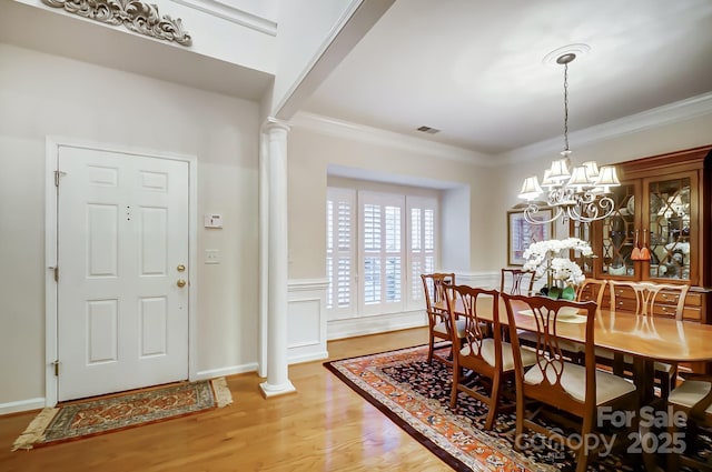 dining space with ornate columns, hardwood / wood-style flooring, ornamental molding, and a notable chandelier