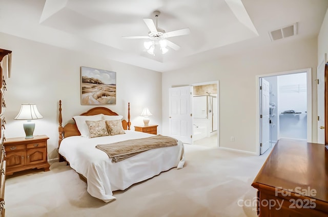 carpeted bedroom with ensuite bathroom, ceiling fan, and a tray ceiling