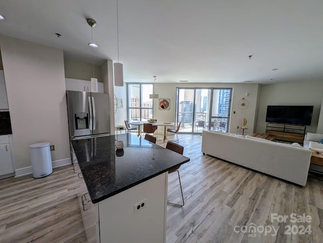 kitchen with pendant lighting, stainless steel fridge with ice dispenser, a kitchen bar, light wood-type flooring, and dark stone counters