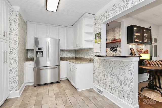 kitchen featuring decorative backsplash, stainless steel refrigerator with ice dispenser, kitchen peninsula, dark stone counters, and white cabinets