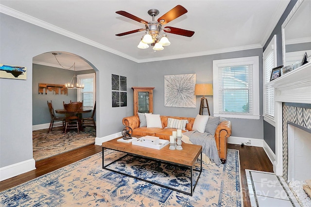 living room with a tiled fireplace, wood-type flooring, ceiling fan with notable chandelier, and ornamental molding