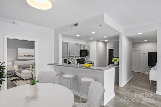 kitchen with a kitchen bar, kitchen peninsula, decorative backsplash, gray cabinets, and black appliances