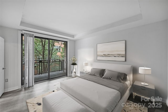 bedroom with a raised ceiling, wood-type flooring, and access to exterior