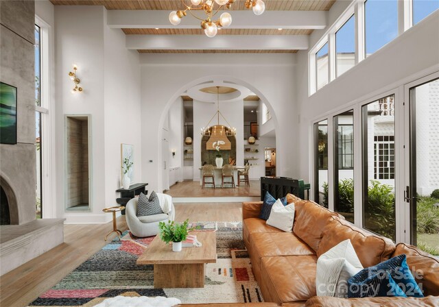 living room with light wood-type flooring, beam ceiling, a notable chandelier, and a high ceiling