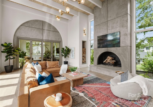 living room featuring a fireplace, wood-type flooring, beam ceiling, and a notable chandelier