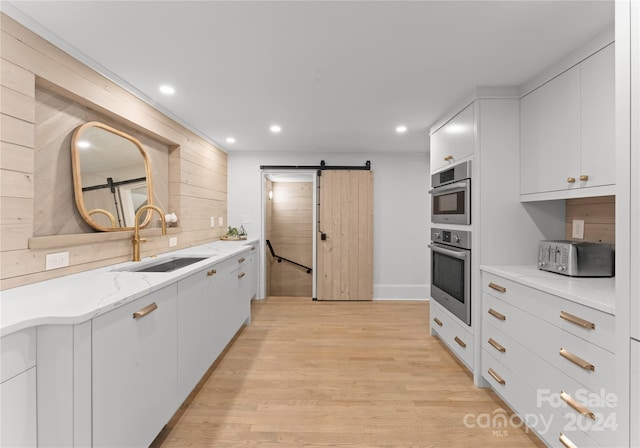 kitchen featuring light wood-type flooring, white cabinetry, sink, light stone countertops, and a barn door