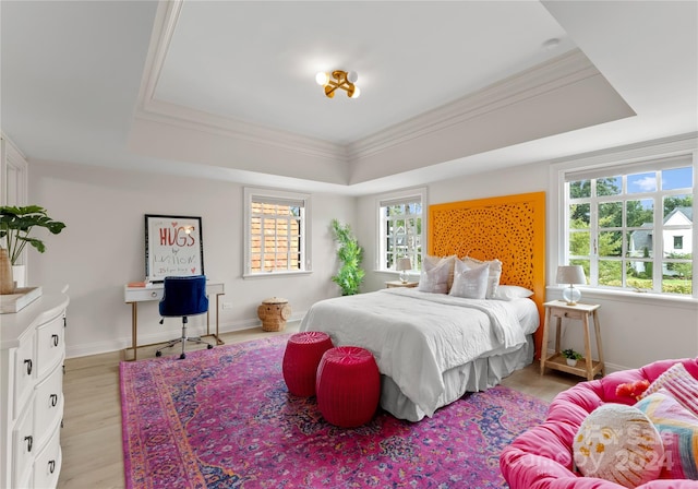 bedroom featuring multiple windows, a tray ceiling, and light hardwood / wood-style flooring