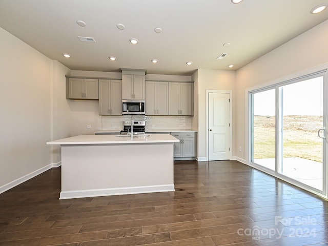 kitchen featuring dark hardwood / wood-style flooring, gray cabinetry, appliances with stainless steel finishes, and a center island with sink