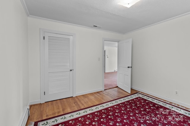 unfurnished bedroom featuring light wood-type flooring, a baseboard heating unit, a closet, ornamental molding, and a textured ceiling