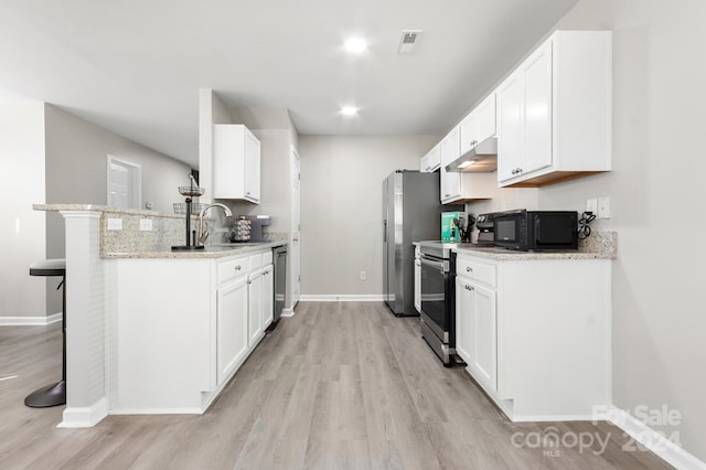 kitchen with appliances with stainless steel finishes, white cabinets, a kitchen breakfast bar, and light stone countertops