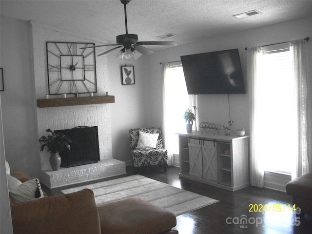 living room featuring ceiling fan, a textured ceiling, a fireplace, and dark hardwood / wood-style flooring