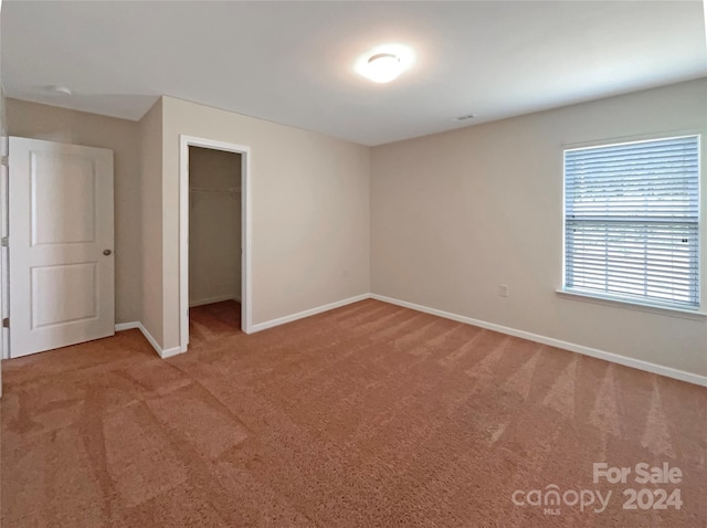 unfurnished bedroom featuring a closet, carpet flooring, a walk in closet, and baseboards