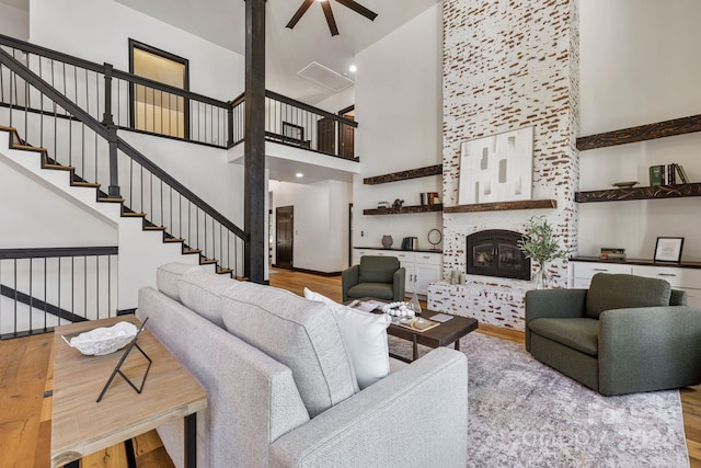 living room featuring light hardwood / wood-style floors, a towering ceiling, ceiling fan, and a large fireplace