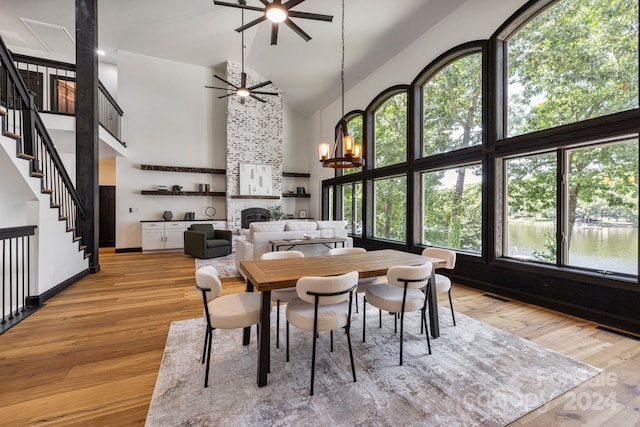 dining space with ceiling fan with notable chandelier, light hardwood / wood-style floors, a large fireplace, and high vaulted ceiling